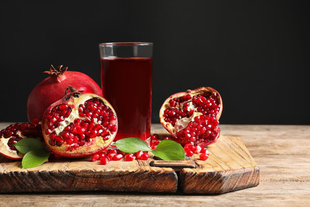 Glass of pomegranate juice and fresh fruits on wooden board against black background, space for textの写真素材