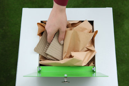 Woman putting cardboard into trash bin on color background, closeup. Recycling conceptの写真素材