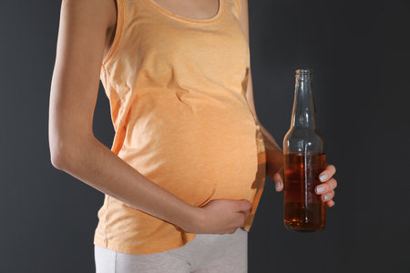 Future mother with bottle of alcohol drink on black background, closeup. Bad habits during pregnancyの写真素材