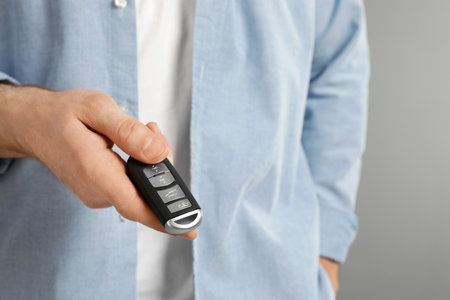 Young man holding car smart key on gray background, closeupの写真素材