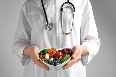 Doctor holding bowl with products for heart-healthy diet on color background, closeupの写真素材