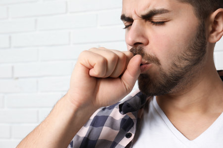 Handsome young man coughing near brick wallの写真素材