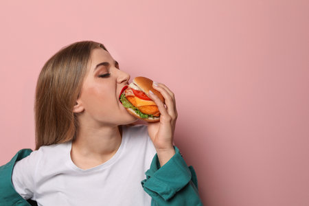 Pretty woman eating tasty burger on color background. Space for textの写真素材