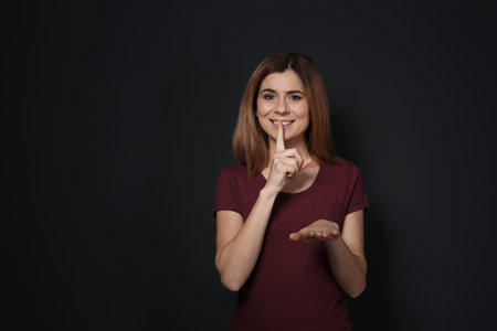 Woman showing HUSH gesture in sign language on black background, space for textの写真素材