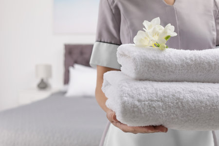 Maid holding fresh towels with flowers in hotel room, closeupの写真素材