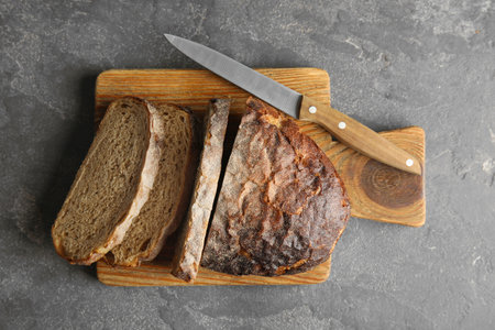 Board with bread and knife on gray background, top view
