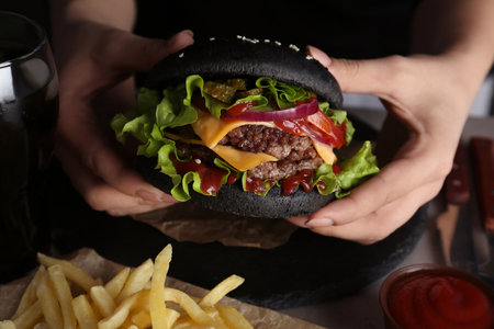 Woman holding tasty black burger at table, closeupの写真素材