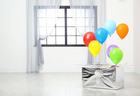 Gift box with bright air balloons on floor indoors. Space for textの写真素材