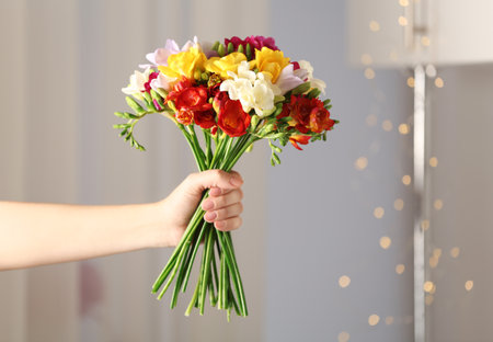 Woman holding bouquet of beautiful spring freesia flowers in roomの写真素材