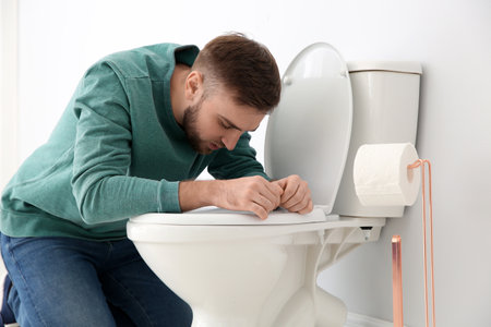 Young man suffering from nausea over toilet bowl indoorsの写真素材