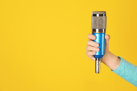 Child holding microphone on color background, closeup of hand. Space for textの写真素材