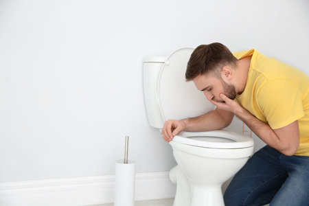 Young man suffering from nausea over toilet bowl indoors