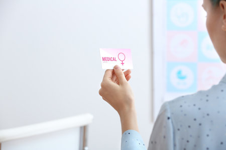 Girl holding medical business card indoors, closeup. Women's health servicesの写真素材
