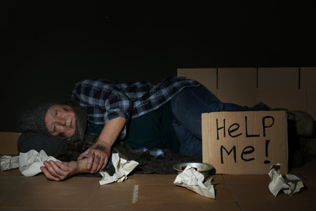 Poor man senior lying near cardboard sign HELP ME on floor