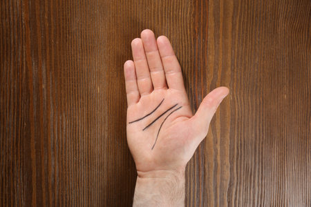 Man showing palm with drawn lines on wooden background, top view. Chiromancy and foretellingの写真素材