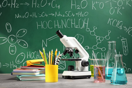 Laboratory glassware, microscope and stationery on table near chalkboard. Chemistry conceptの写真素材