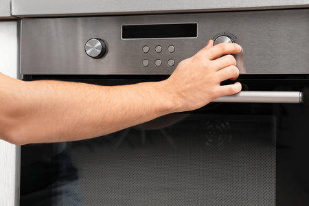 Young man adjusting oven settings in kitchen, closeupの写真素材