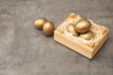 Wooden crate with golden eggs on table, space for textの写真素材