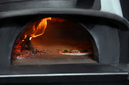 Burning firewood and tasty pizza in oven at restaurant kitchenの写真素材