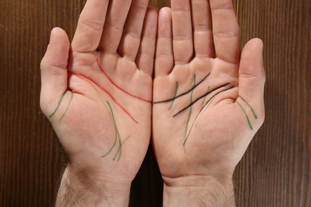 Man showing palms with drawn lines on wooden background, top view. Chiromancy and foretellingの写真素材