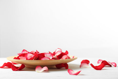 Wooden plate with rose petals on table against white background. Space for textの写真素材