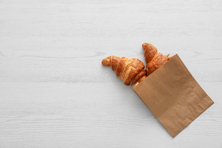 Paper bag with pastry on light wooden background, top view with space for textの写真素材