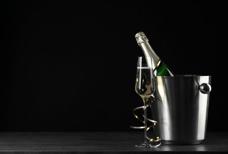 Glass of champagne near bucket with bottle on black background, space for textの写真素材