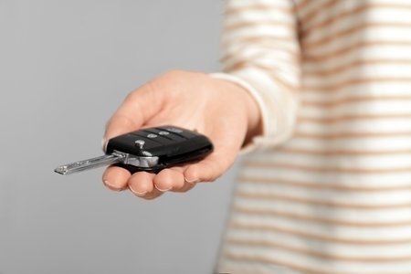 Young woman holding car key on gray background, closeupの写真素材