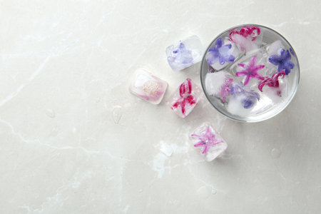 Glass of water and ice cubes with flowers on table, top view. Space for textの写真素材