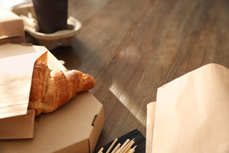 Paper bag with pastry and takeaway food on wooden table. Space for textの写真素材