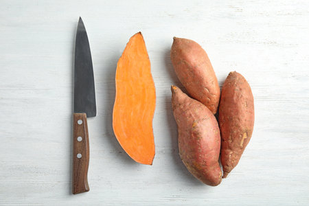 Flat lay composition with sweet potatoes and knife on white wooden backgroundの写真素材
