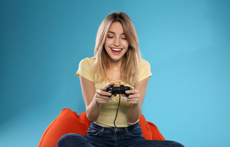 Emotional young woman playing video games with controller on color background