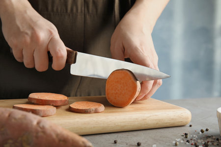 Woman cutting sweet potato on wooden board, closeupの写真素材