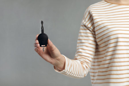 Young woman holding car key on gray background, closeup