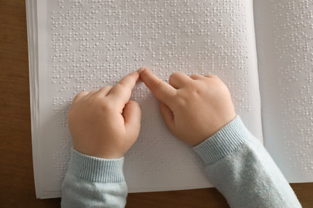 Blind child reading book written in Braille at table, top viewの写真素材