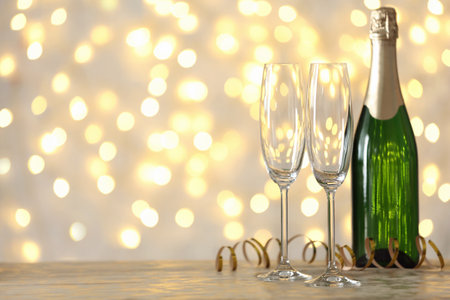 Empty glasses and bottle of champagne on table against blurred lights. Space for textの写真素材
