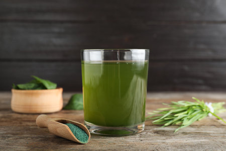 Glass of spirulina drink, scoop with powder and wheat grass on wooden tableの写真素材