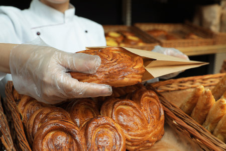 Baker putting fresh bun into paper bag, closeupの写真素材