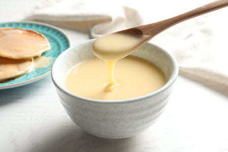 Spoon of pouring condensed milk over bowl on table, closeup. Dairy productsの写真素材