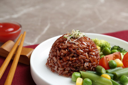 Plate of boiled brown rice with vegetables served on table, closeup. Space for textの写真素材