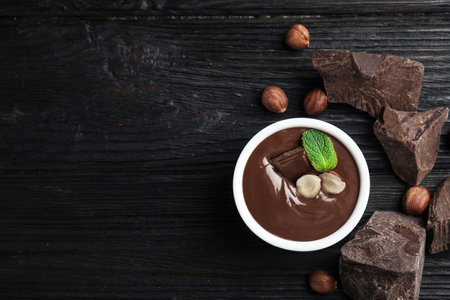 Dessert bowl with sweet chocolate cream, nuts and chunks on wooden table, flat lay. Space for textの写真素材