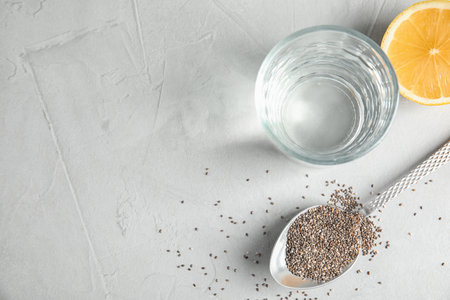 Spoon with chia seeds and glass of water on gray background, flat lay. Space for textの写真素材