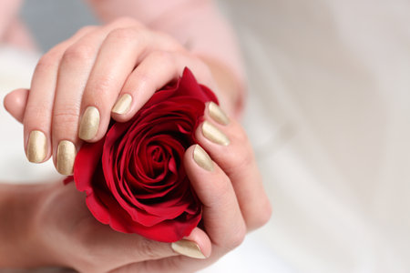 Woman with gold manicure holding rose on blurred background, closeup. Nail polish trendsの写真素材