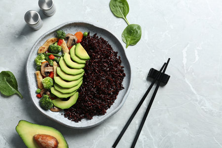 Plate of boiled brown rice with avocado served on table, top view. Space for text