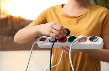 Woman inserting power plug into extension cord indoors, closeup. Electrician's professional...