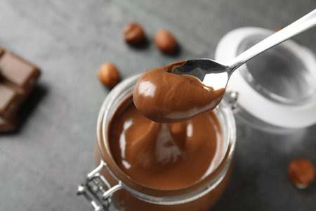 Spoon with tasty chocolate cream over full jar on table, view from aboveの写真素材