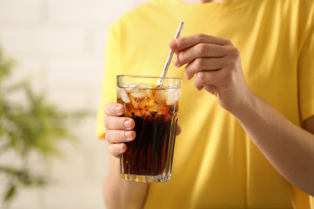 Woman holding glass of cola with ice on blurred background, closeup. Space for textの写真素材