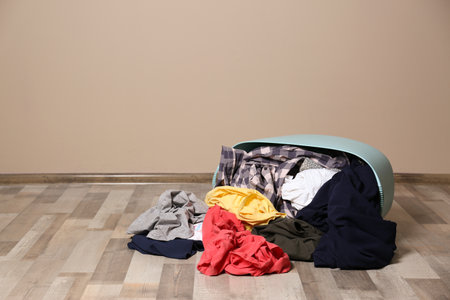 Dirty clothes scattered from laundry basket on floor indoors. Space for textの写真素材