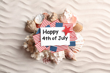 Flat lay composition with greeting card, USA flags and seashells on sand. Happy Independence Dayの写真素材