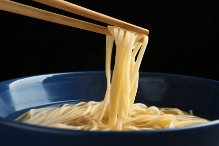 Eating noodle dish with chopsticks against black background, closeupの写真素材